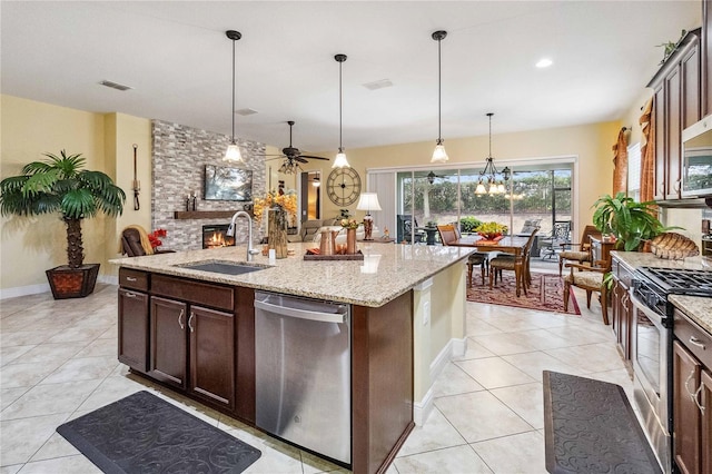 kitchen with sink, stainless steel appliances, dark brown cabinetry, light stone counters, and a fireplace