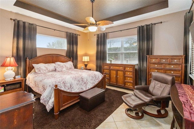 bedroom with ceiling fan, a raised ceiling, tile patterned flooring, and a textured ceiling