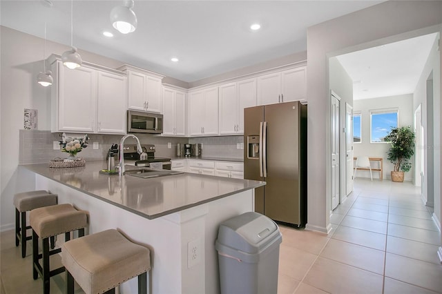 kitchen with white cabinets, a kitchen bar, hanging light fixtures, kitchen peninsula, and stainless steel appliances