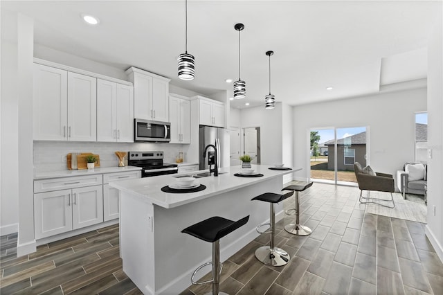 kitchen with white cabinetry, appliances with stainless steel finishes, a kitchen island with sink, and decorative light fixtures