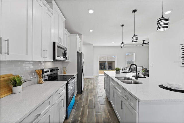 kitchen with sink, appliances with stainless steel finishes, white cabinetry, hanging light fixtures, and light stone countertops