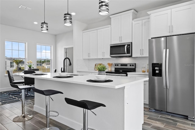 kitchen with stainless steel appliances, decorative light fixtures, a center island with sink, and white cabinets