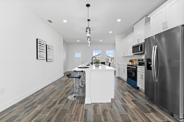 kitchen featuring appliances with stainless steel finishes, pendant lighting, an island with sink, white cabinets, and a kitchen bar