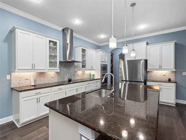 kitchen featuring sink, hanging light fixtures, stainless steel appliances, a center island with sink, and wall chimney range hood