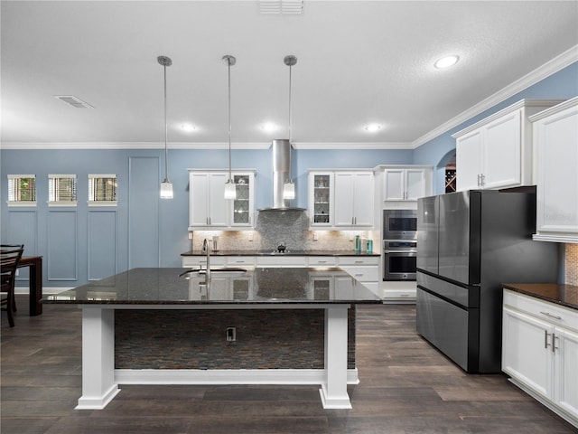 kitchen with appliances with stainless steel finishes, decorative light fixtures, a kitchen island with sink, and wall chimney range hood