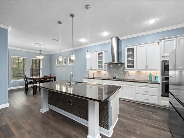 kitchen with an island with sink, sink, wall chimney range hood, and decorative light fixtures