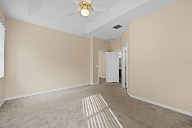 empty room with ceiling fan, a raised ceiling, and light carpet