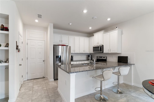 kitchen featuring sink, appliances with stainless steel finishes, white cabinetry, dark stone countertops, and kitchen peninsula