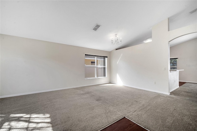 carpeted empty room featuring a notable chandelier and vaulted ceiling