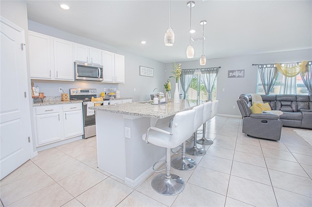 kitchen featuring light stone counters, hanging light fixtures, an island with sink, stainless steel appliances, and white cabinets