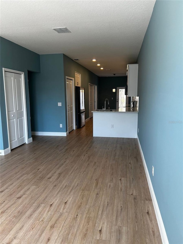 unfurnished living room with sink, a textured ceiling, and light wood-type flooring