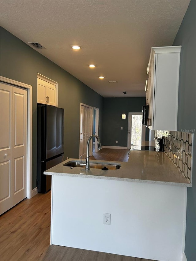 kitchen with black refrigerator, sink, kitchen peninsula, and white cabinets