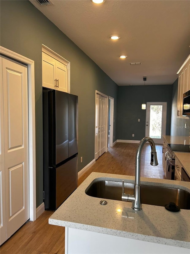 kitchen with stainless steel electric range oven, sink, hanging light fixtures, black fridge, and light hardwood / wood-style flooring