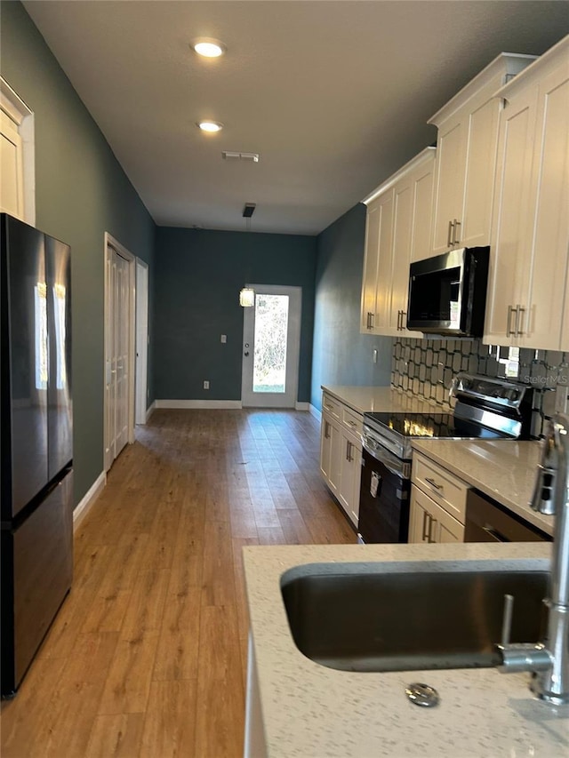 kitchen with refrigerator, light hardwood / wood-style flooring, black / electric stove, pendant lighting, and white cabinets