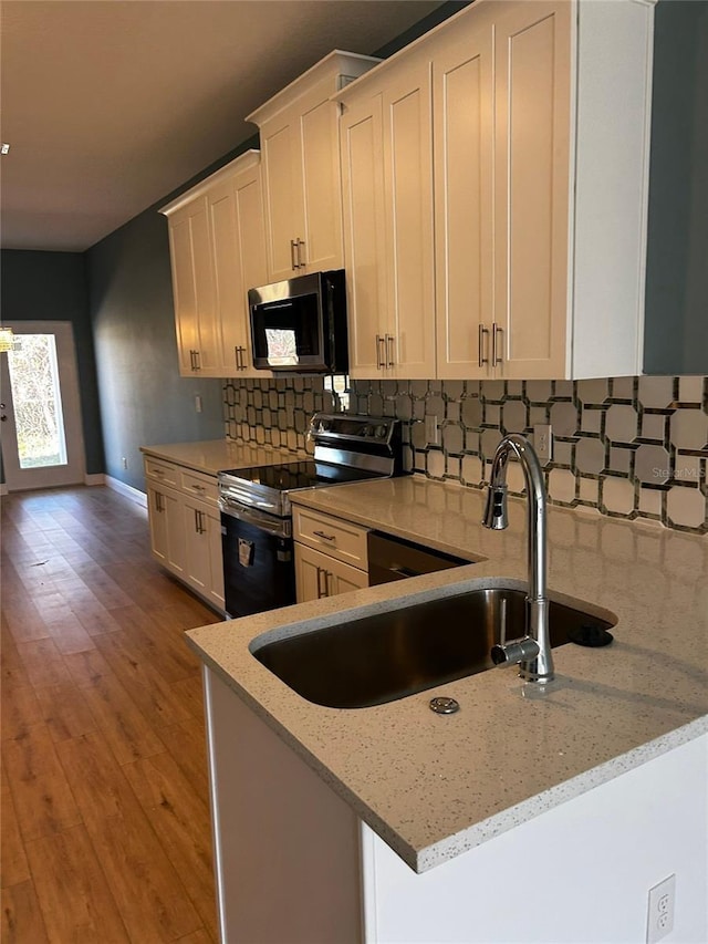 kitchen with stainless steel electric stove, white cabinets, backsplash, light stone counters, and kitchen peninsula