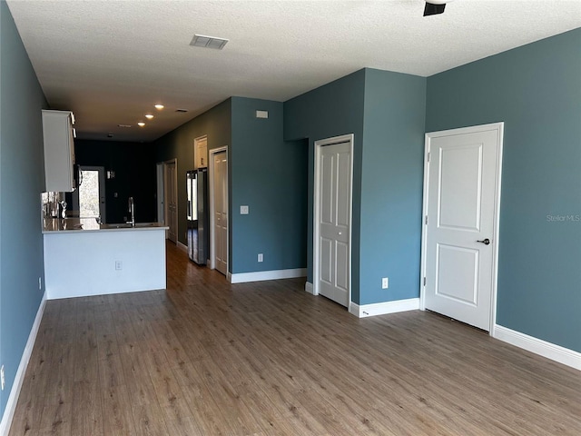 unfurnished living room with hardwood / wood-style floors, sink, and a textured ceiling