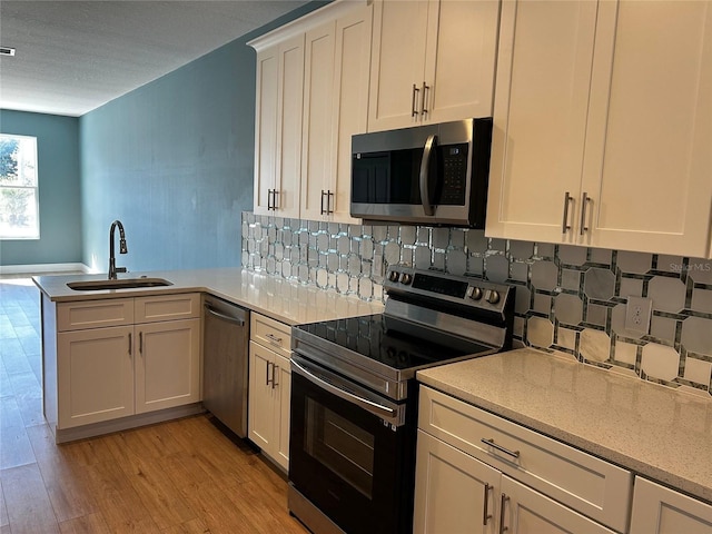 kitchen with sink, appliances with stainless steel finishes, kitchen peninsula, white cabinets, and backsplash