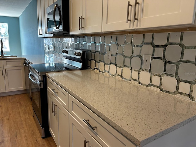 kitchen with appliances with stainless steel finishes, sink, white cabinets, decorative backsplash, and light hardwood / wood-style flooring