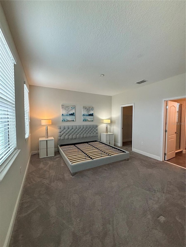 unfurnished bedroom with dark colored carpet, a spacious closet, a textured ceiling, and a closet