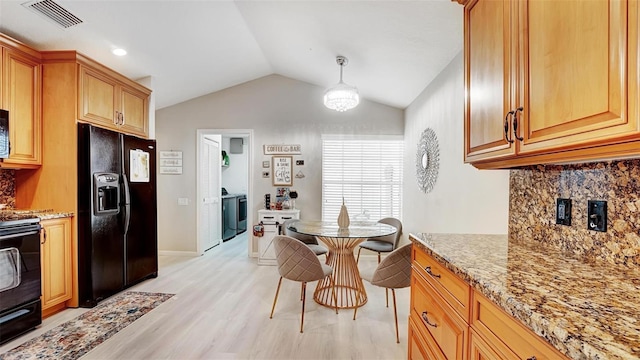 kitchen featuring lofted ceiling, black fridge, decorative light fixtures, light stone countertops, and decorative backsplash