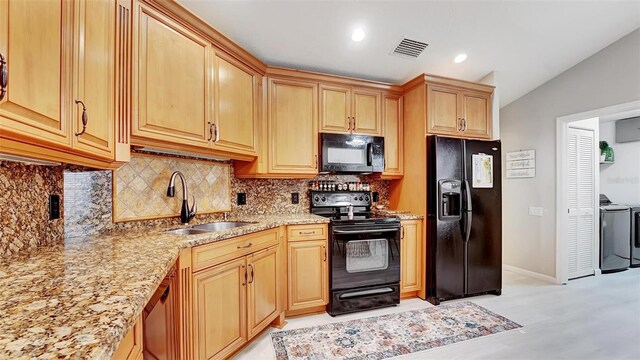 kitchen featuring lofted ceiling, sink, light stone counters, washing machine and dryer, and black appliances