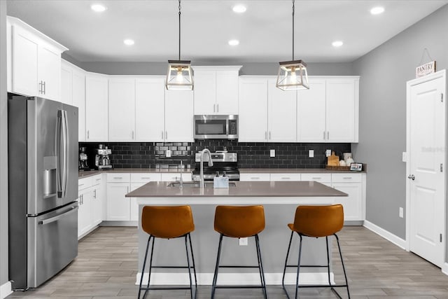 kitchen with appliances with stainless steel finishes, decorative light fixtures, and a center island with sink