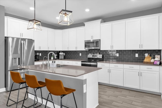 kitchen featuring pendant lighting, sink, appliances with stainless steel finishes, a kitchen breakfast bar, and white cabinets