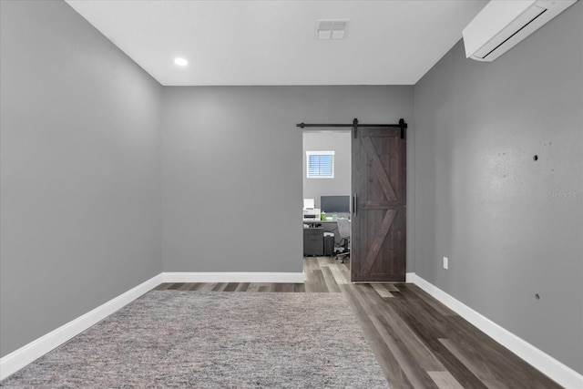 empty room with dark wood-type flooring, a wall mounted air conditioner, and a barn door