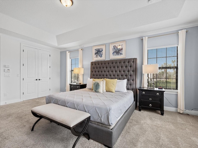 carpeted bedroom with a tray ceiling, ornamental molding, and a closet