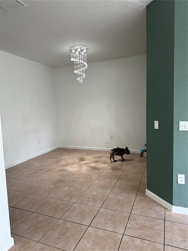 spare room featuring light tile patterned floors, a textured ceiling, and a chandelier