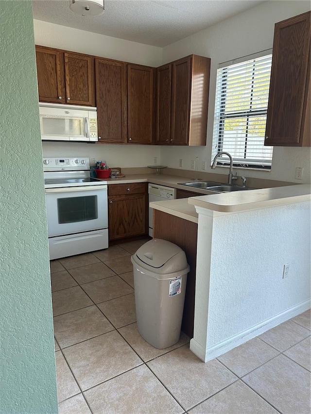 kitchen featuring sink, light tile patterned floors, white appliances, and kitchen peninsula