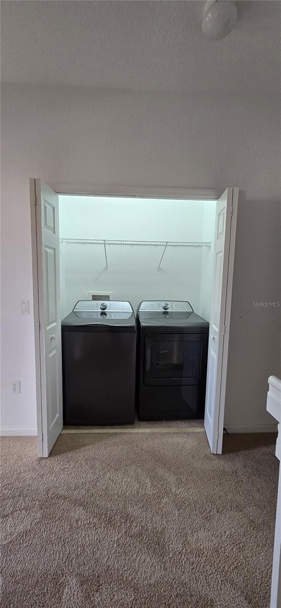 laundry area featuring washer and clothes dryer, light colored carpet, and a textured ceiling