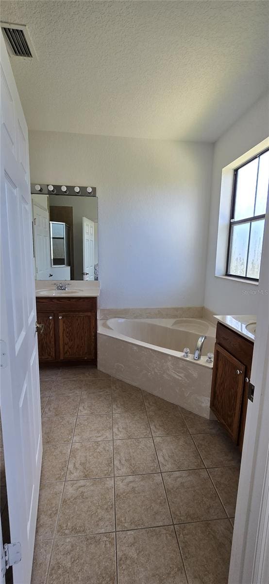 bathroom with tile patterned floors, a tub to relax in, vanity, and a textured ceiling