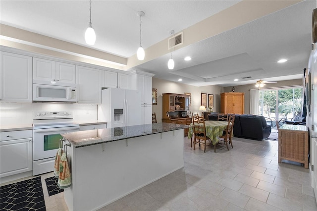 kitchen with a kitchen island, decorative light fixtures, white cabinets, a raised ceiling, and white appliances