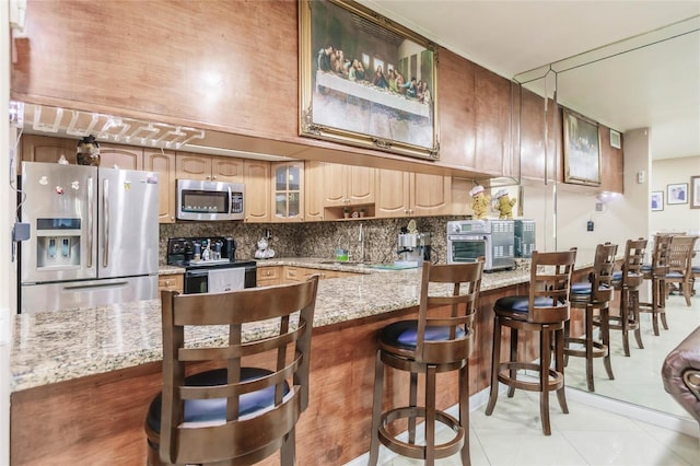 kitchen with light tile patterned floors, a breakfast bar area, stainless steel appliances, light stone counters, and decorative backsplash