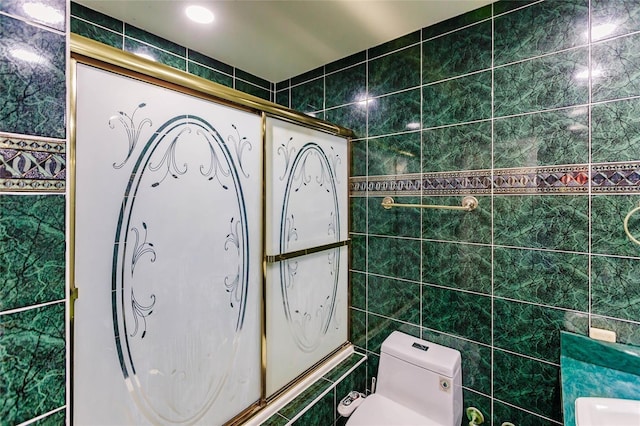 bathroom with tile walls, shower / bath combination with glass door, and toilet