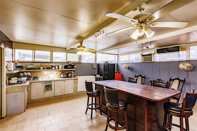 kitchen featuring a wall mounted AC, a kitchen breakfast bar, beamed ceiling, ceiling fan, and white cabinets