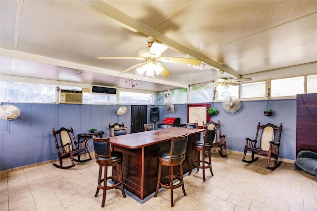 interior space featuring ceiling fan, a kitchen bar, beam ceiling, and a wall unit AC