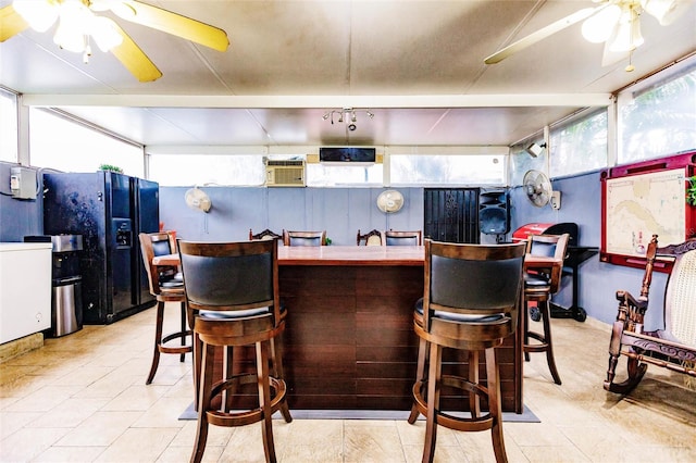 kitchen featuring ceiling fan, a breakfast bar, and black fridge with ice dispenser