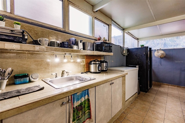 kitchen with black refrigerator, sink, light tile patterned floors, and decorative backsplash