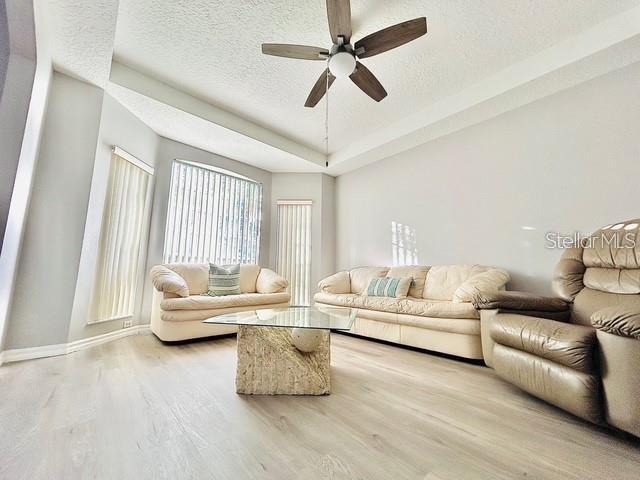 living room featuring hardwood / wood-style floors, a tray ceiling, a textured ceiling, and ceiling fan