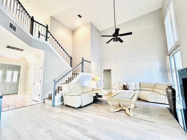 living room with a high ceiling, ceiling fan, and light hardwood / wood-style floors