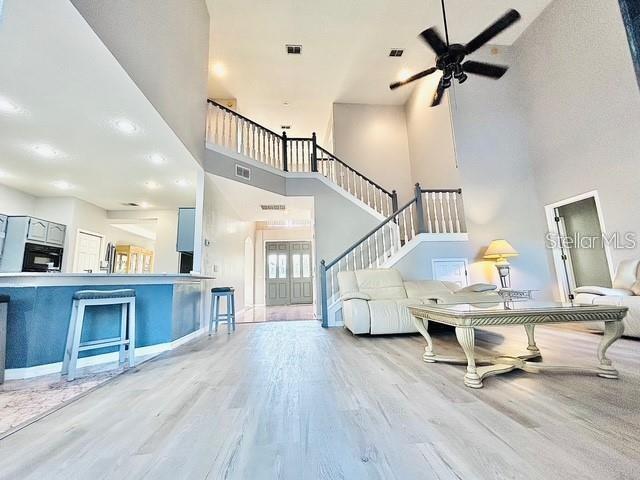 living room featuring light wood finished floors, visible vents, a high ceiling, and stairway