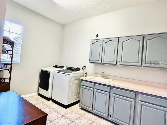 laundry room featuring sink, cabinets, washer and clothes dryer, light tile patterned floors, and a textured ceiling