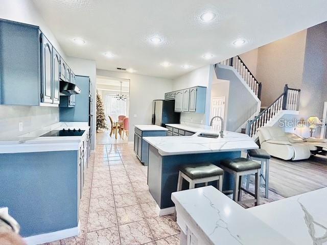 kitchen with stainless steel refrigerator, sink, gray cabinetry, a kitchen bar, and kitchen peninsula