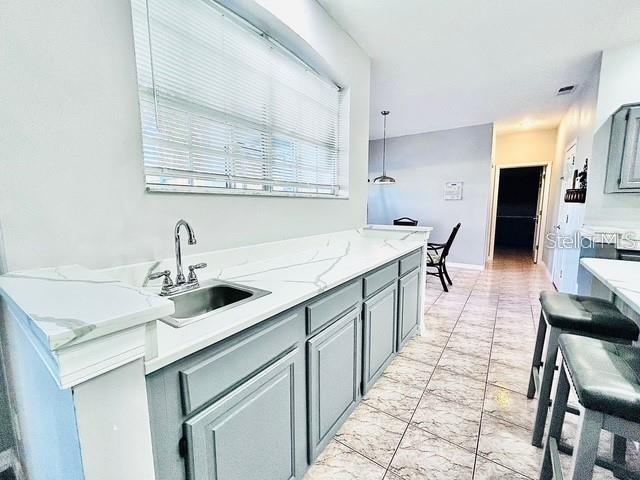 kitchen with pendant lighting, sink, gray cabinetry, and light stone countertops