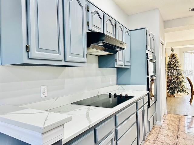 kitchen with black electric cooktop, double oven, and light stone countertops