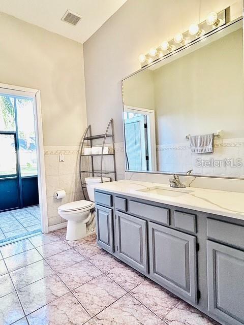 bathroom with tile patterned flooring, vanity, tile walls, and toilet