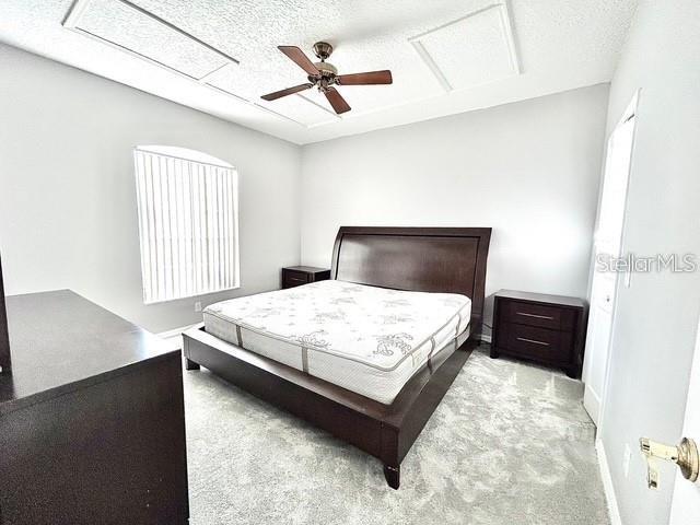 bedroom with ceiling fan, light colored carpet, and a textured ceiling