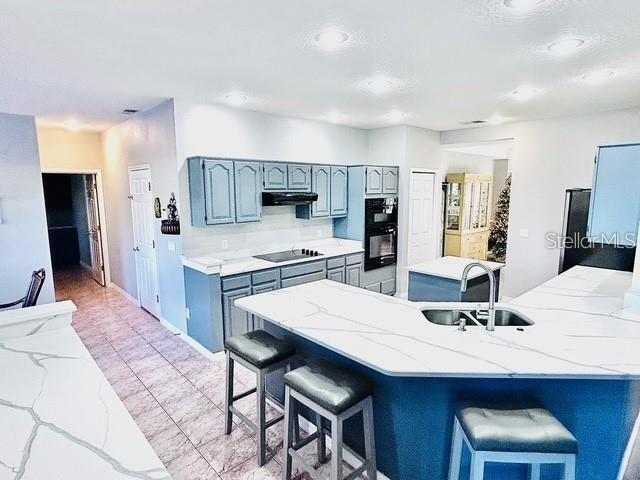 kitchen featuring light tile patterned floors, a kitchen breakfast bar, under cabinet range hood, black appliances, and a sink